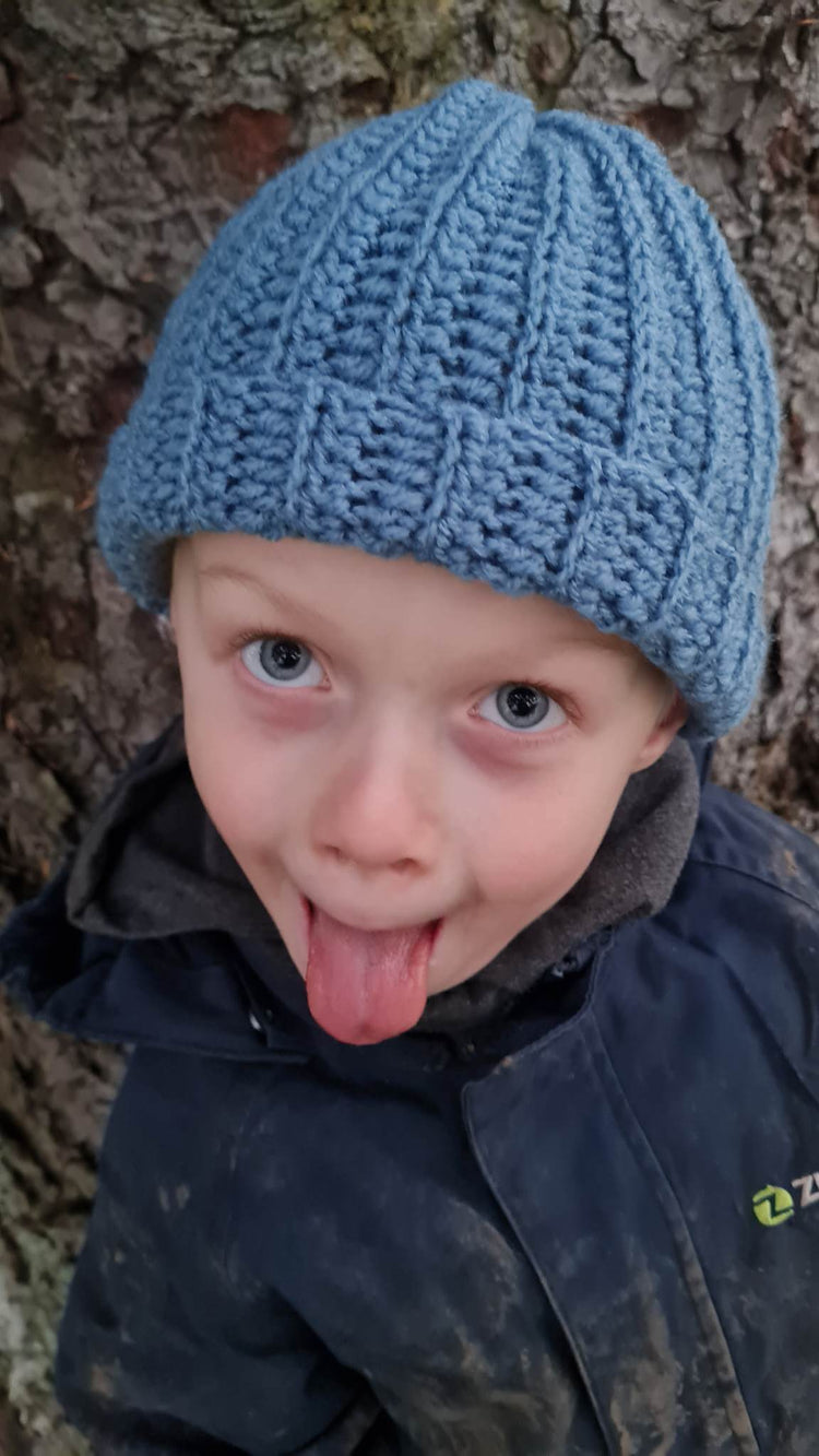 Funny little child putting his tongue out, wearing a crocheted hat, outside