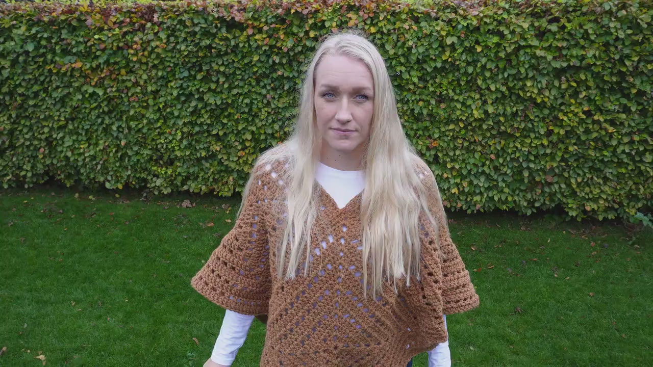 short video of woman, outside, crocheted poncho, made of granny squares, green grass, green hedge