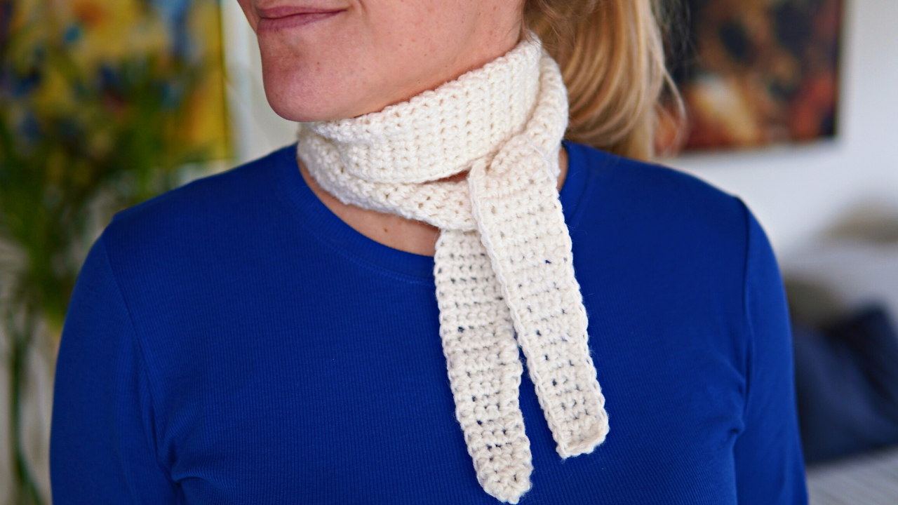 Young woman in a blue shirt wearing a crocheted little scarf in white mohair/wool yarn