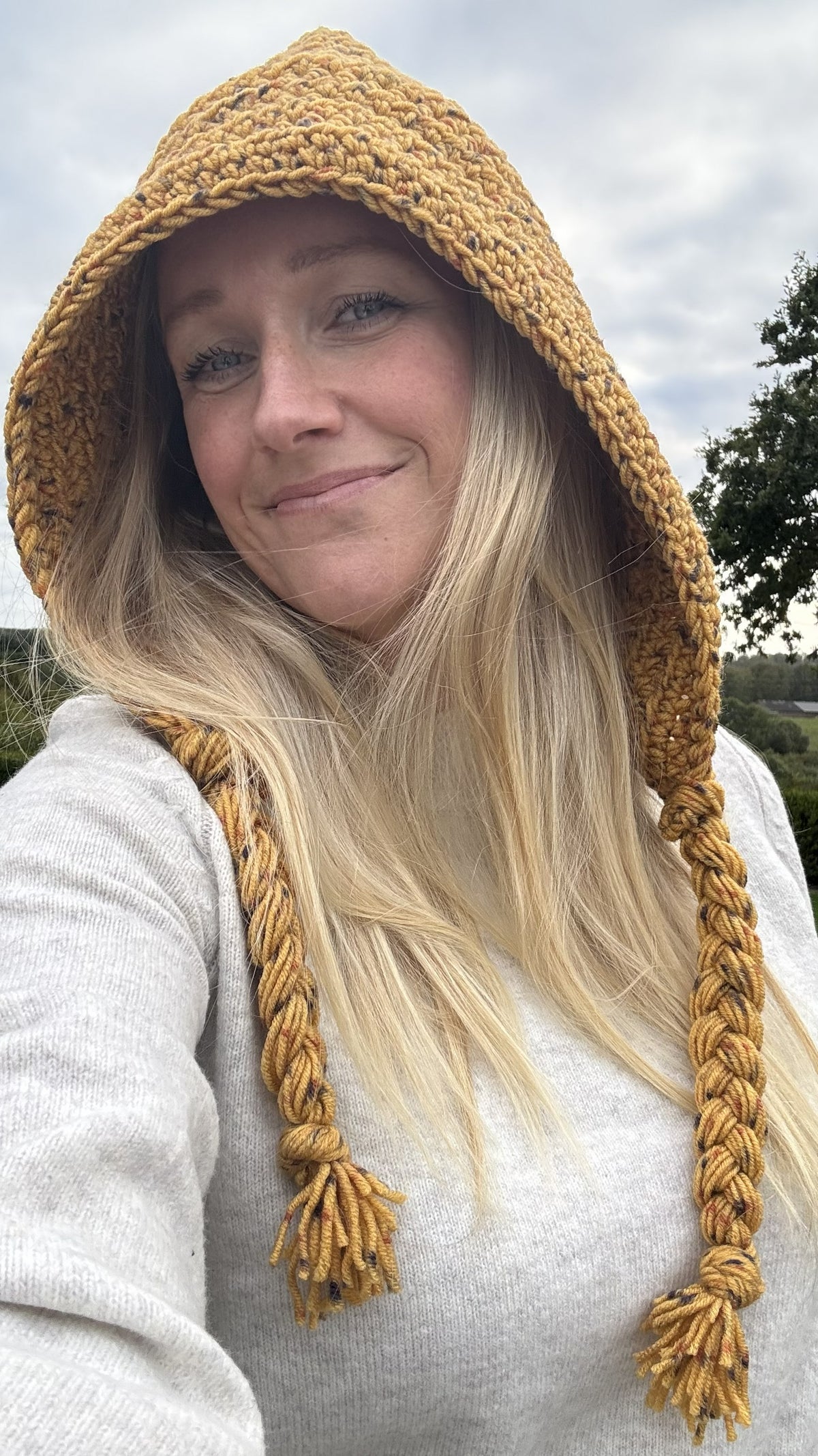 Adult wearing a mustard crochet hood with long braided yarn ties