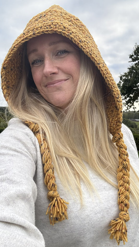 Adult wearing a mustard crochet hood with long braided yarn ties