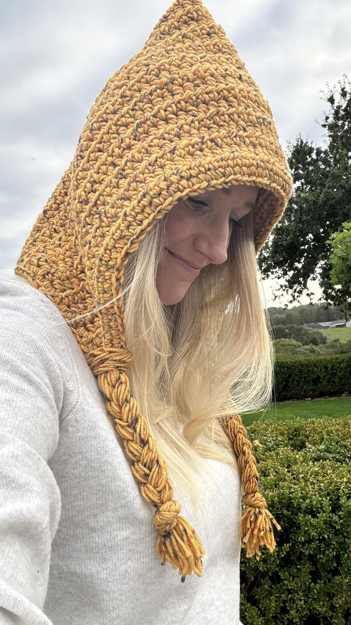 Adult wearing a mustard crochet hood with long braided yarn ties
