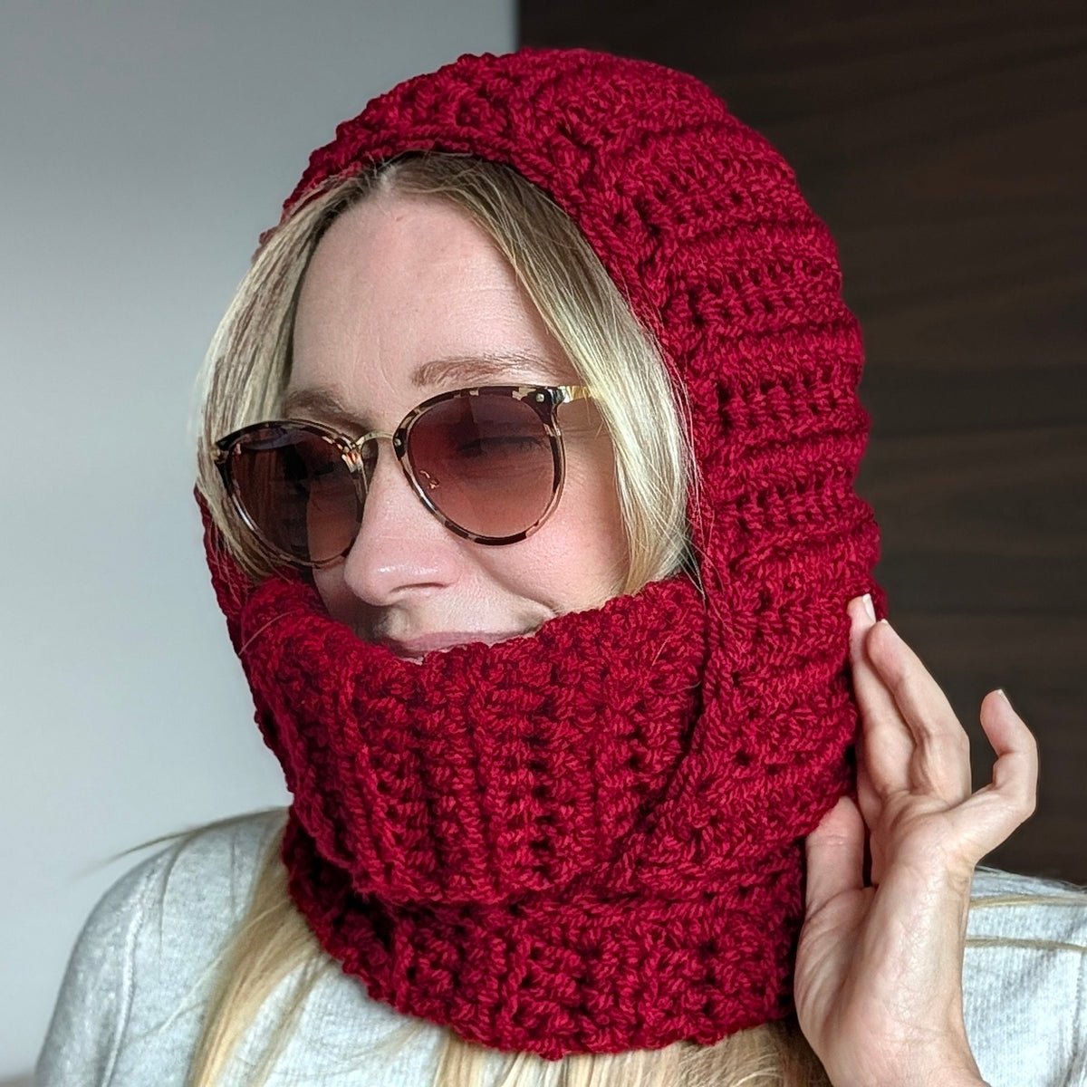 Woman wearing sunglasses and a burgundy crocheted turtleneck hood with chunky ribbed stitches and a face-covering neck section.