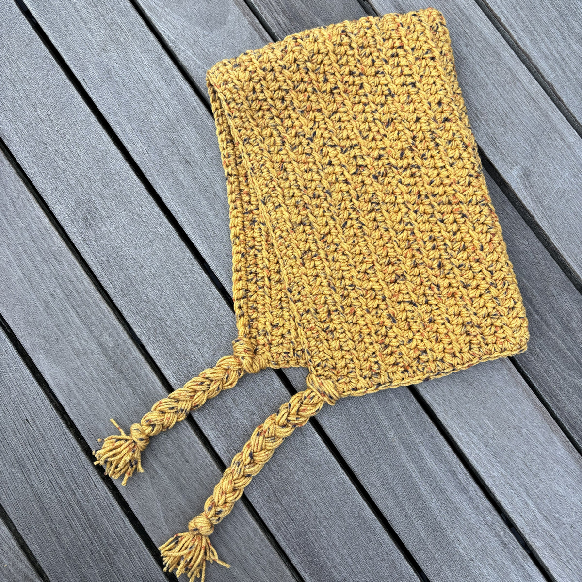 Mustard crochet hood laid flat with long finished braided ties