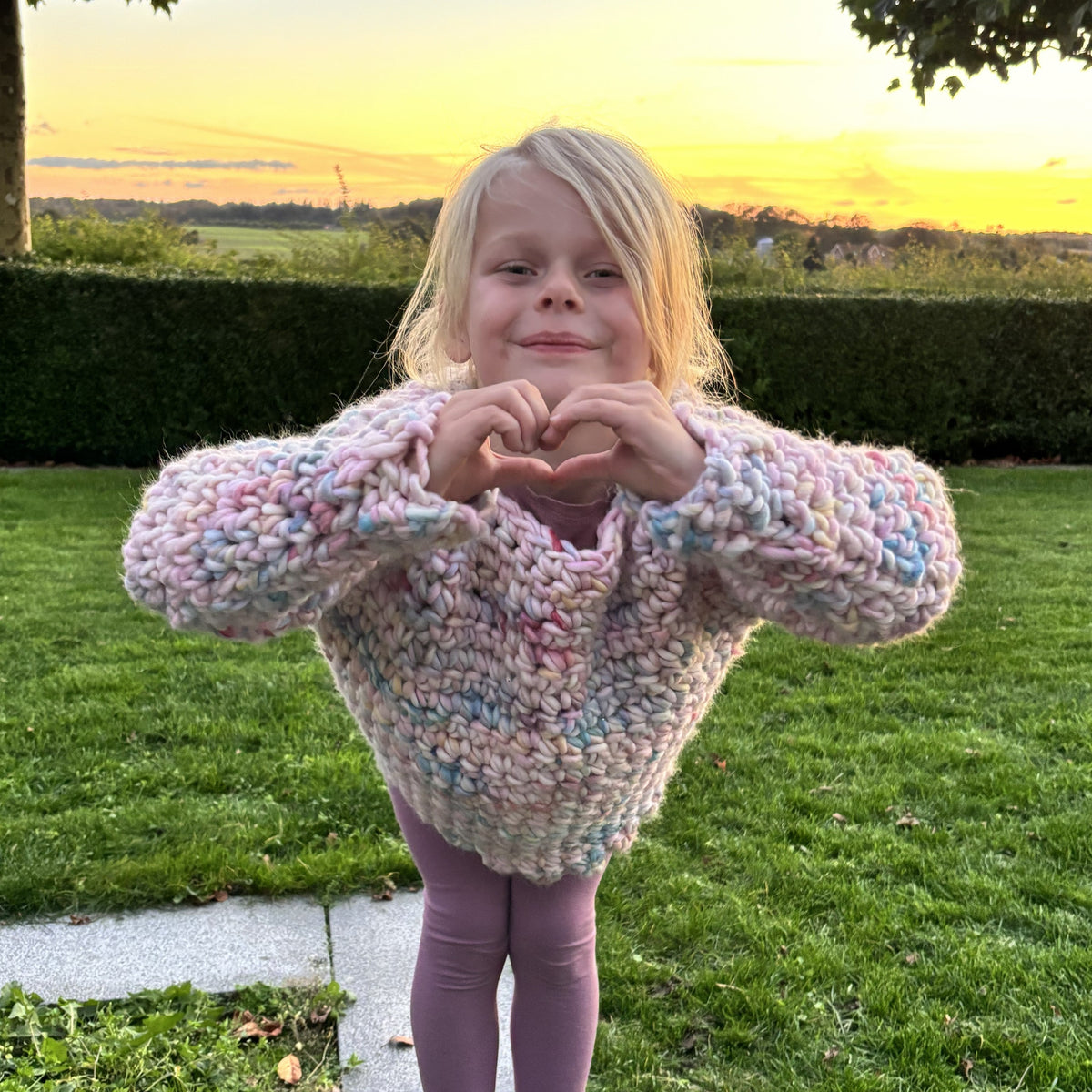 Young girl modeling a chunky pastel crochet sweater with ribbed hem and long sleeves, shown in two playful front poses outdoors.