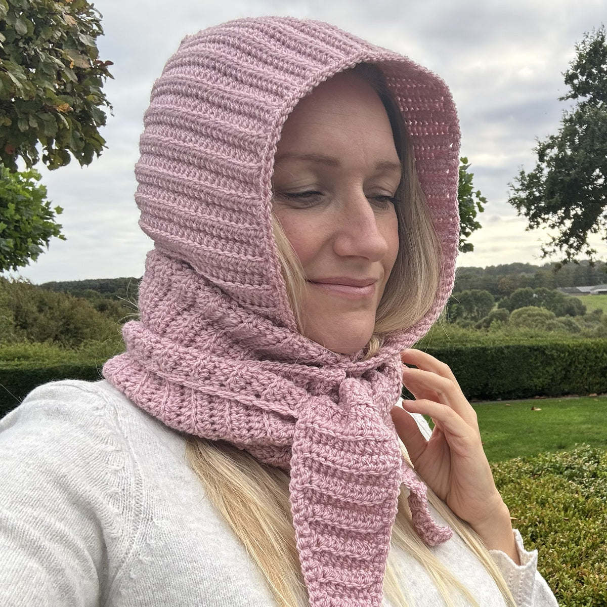 Woman wearing a pink ribbed crochet Sophie Hood with long scarf ties outdoors