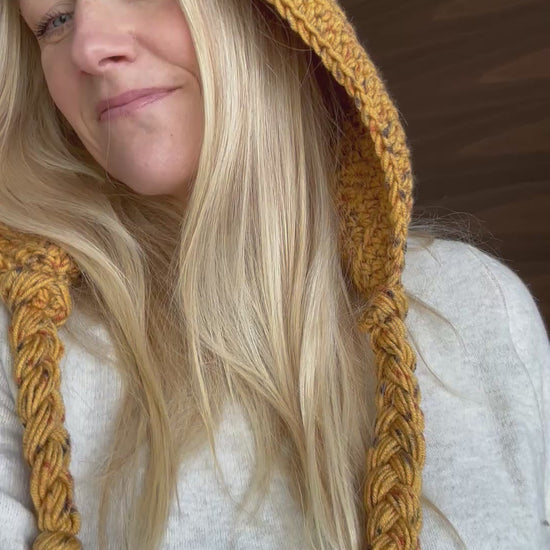 Adult wearing a mustard crochet hood with long braided yarn ties