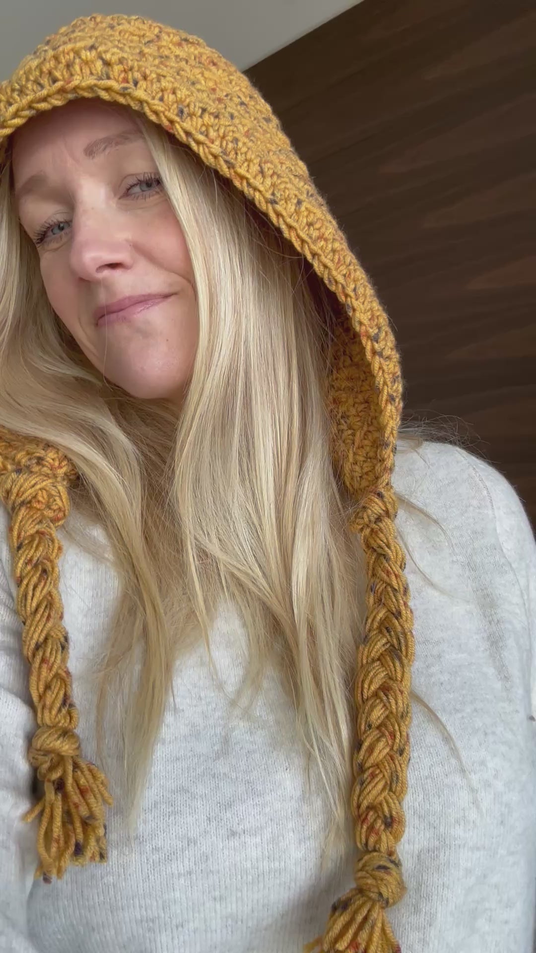 Adult wearing a mustard crochet hood with long braided yarn ties