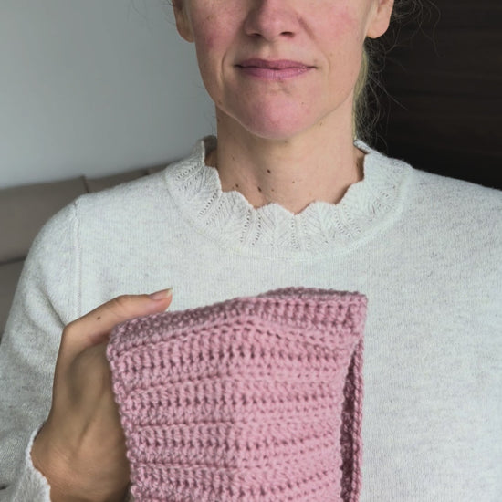 Woman wearing a dusty pink ribbed Sophie Scarf tied around her neck over a cream sweater, with two tapered crochet ends hanging in front.