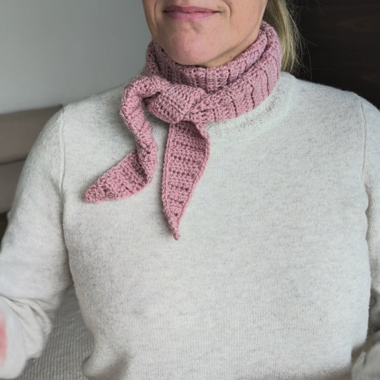 Side view of a woman in a cream knit sweater wearing a pink ribbed crochet neck scarf with the tapered ends tied loosely at the front.