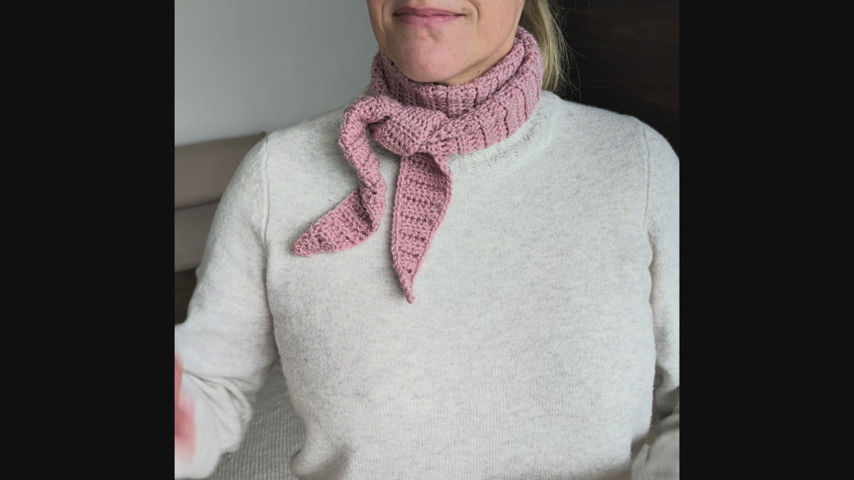 Side view of a woman in a cream knit sweater wearing a pink ribbed crochet neck scarf with the tapered ends tied loosely at the front.